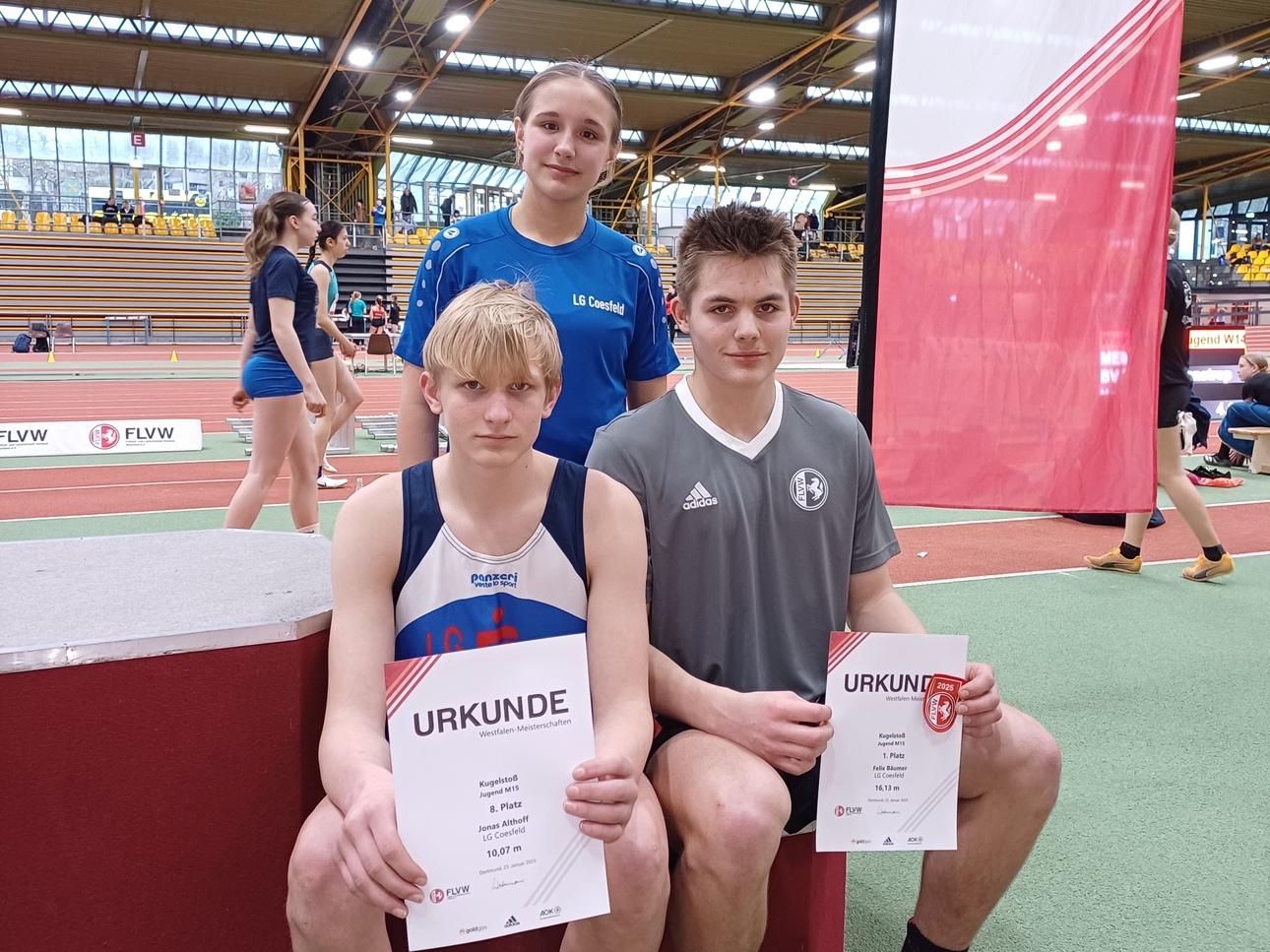 Drei Jugendliche halten Urkunden in einer Sporthalle, umgeben von Sportgeräten und anderen Teilnehmern.