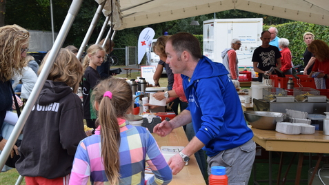 Menschen stehen an einem Tisch unter einem Zelt, um Essen und Getränke bei einer Veranstaltung zu erhalten.