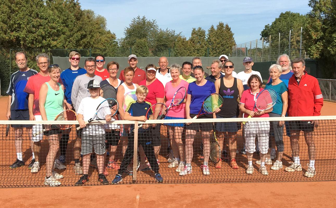 Gruppe von 30 Personen in farbigen Sportoutfits, posierend mit Tennisschlägern auf einem Platz im Freien.