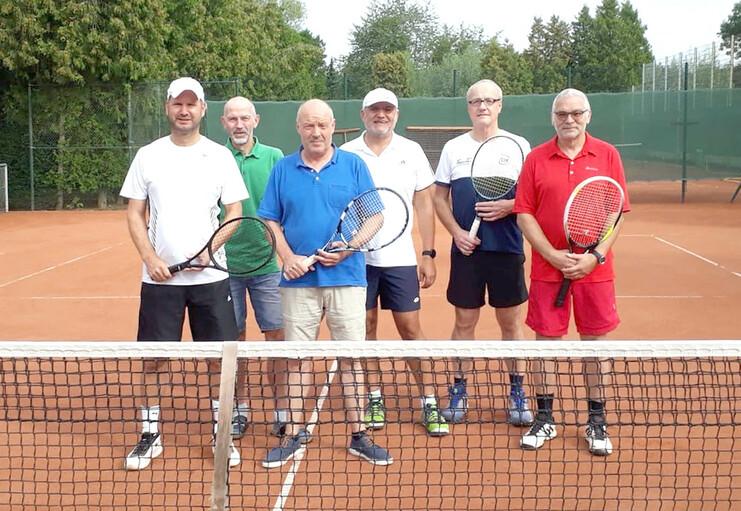 Sechs Männer mit Tennisschlägern stehen am Netz eines Sandtennisplatzes in sportlicher Bekleidung.