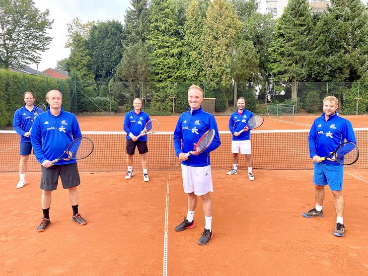 Sechs Männer in blauen Sportjacken mit Tennisschlägern stehen auf einem roten Tennisplatz vor einem Netz.