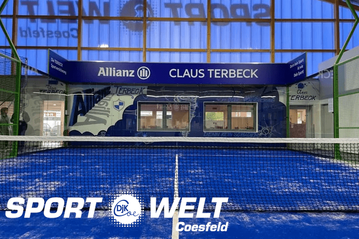 Blick auf einen Padelplatz mit blauer Spielfläche und Sponsorenbanner im Hintergrund.