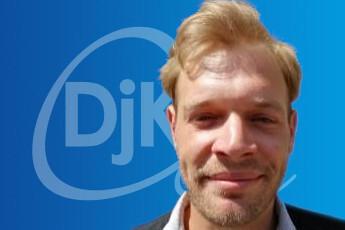 Portrait eines Mannes mit blonden Haaren vor einem blauen Hintergrund mit dem Logo „Djk“ im Hintergrund.