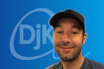 Portrait eines lächelnden Mannes mit zurückgehltem Haar und schwarzer Kappe vor einem blauen Hintergrund mit Logo.