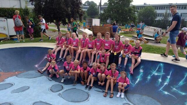 Gruppe von Kindern in pinken T-Shirts sitzt auf einem muralverzierten Skate-Pool in einem Freizeitareal.