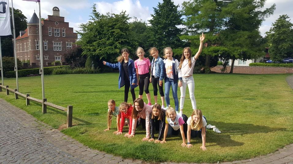 Gruppe von Mädchen posiert im Freien, mehrere stehen oben auf einem kleinen Menschenstapel auf einer Wiese.