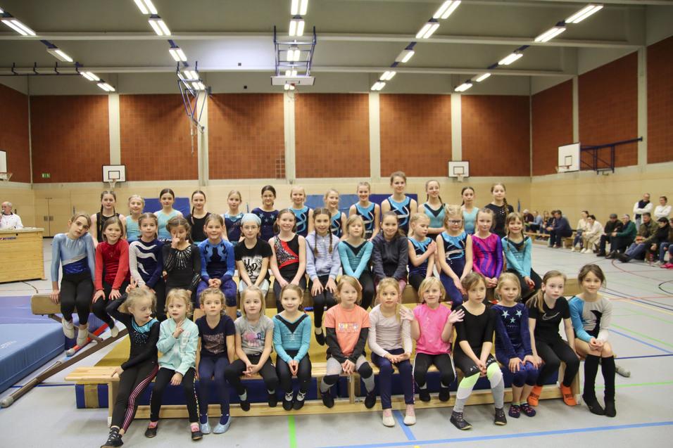 Gruppennahaufnahme von Mädchen in Gymnastikanzügen, die auf einer Sitzbank in einer Sporthalle posieren.