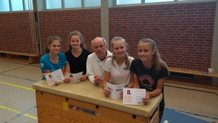 Vier Jugendliche stehen am Turnkasten in einer Sporthalle, halten Urkunden in der Hand, ein Erwachsener sitzt in der Mitte.