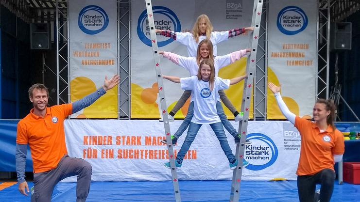 Vier Kinder und zwei Erwachsene posieren auf einer Bühne vor einem Banner der Kampagne „Kinder stark machen“.