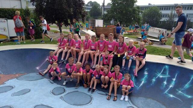 Gruppe von Kindern in pinken T-Shirts sitzt auf einem muralverzierten Skate-Pool in einem Freizeitareal.