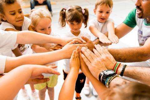 Kinder in T-Shirts legen ihre Hände aufeinander, um Teamgeist in einem spielerischen Moment zu zeigen.