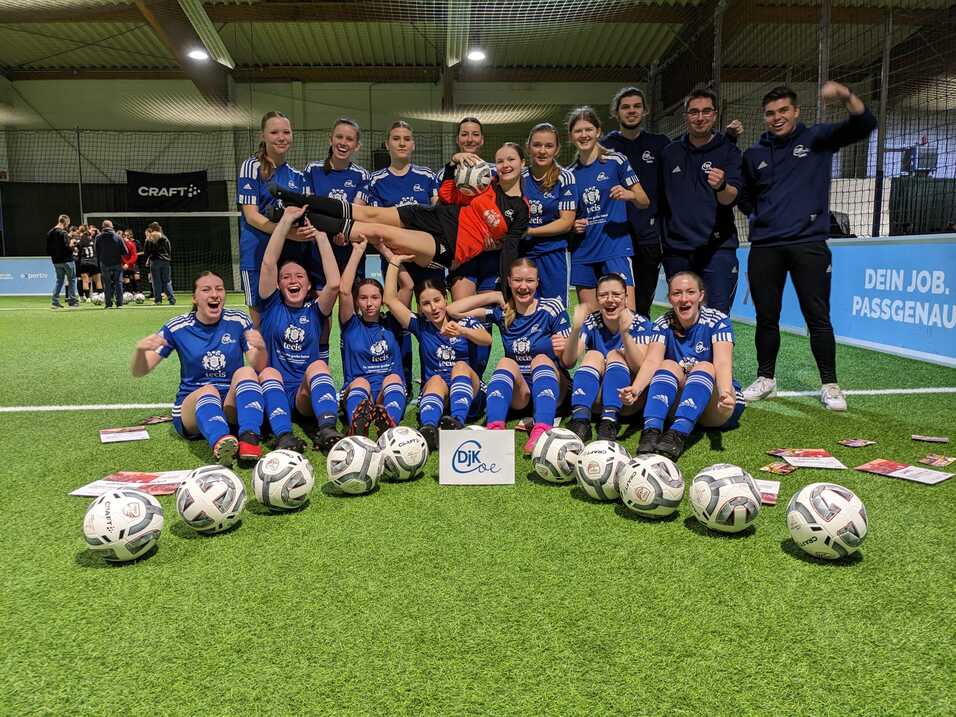 Gruppenfoto eines Jugendfußballteams in blauen Trikots, umringt von Fußball und jubelnden Trainern.