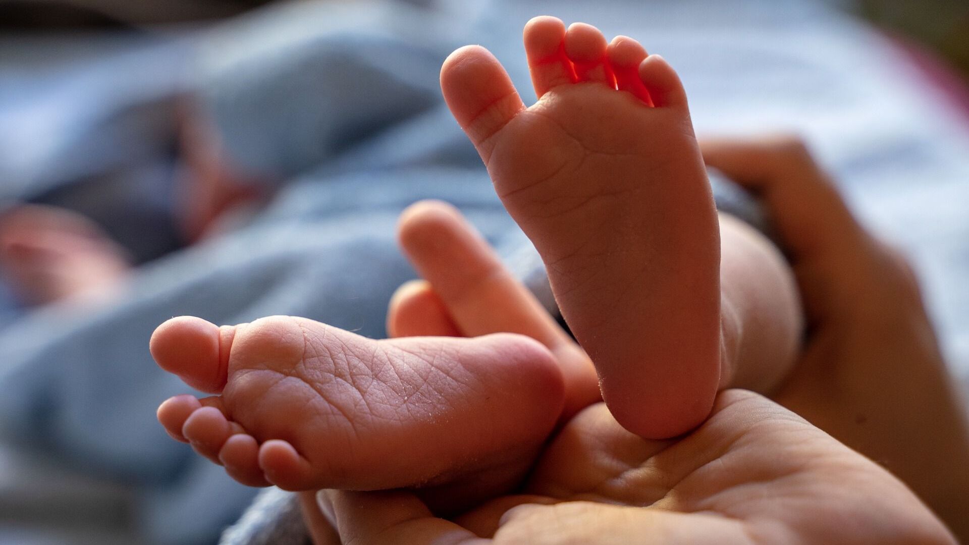 Nahaufnahme von Babyfüßen, die in einer Hand liegen, mit sanften Texturen und weicher Beleuchtung.