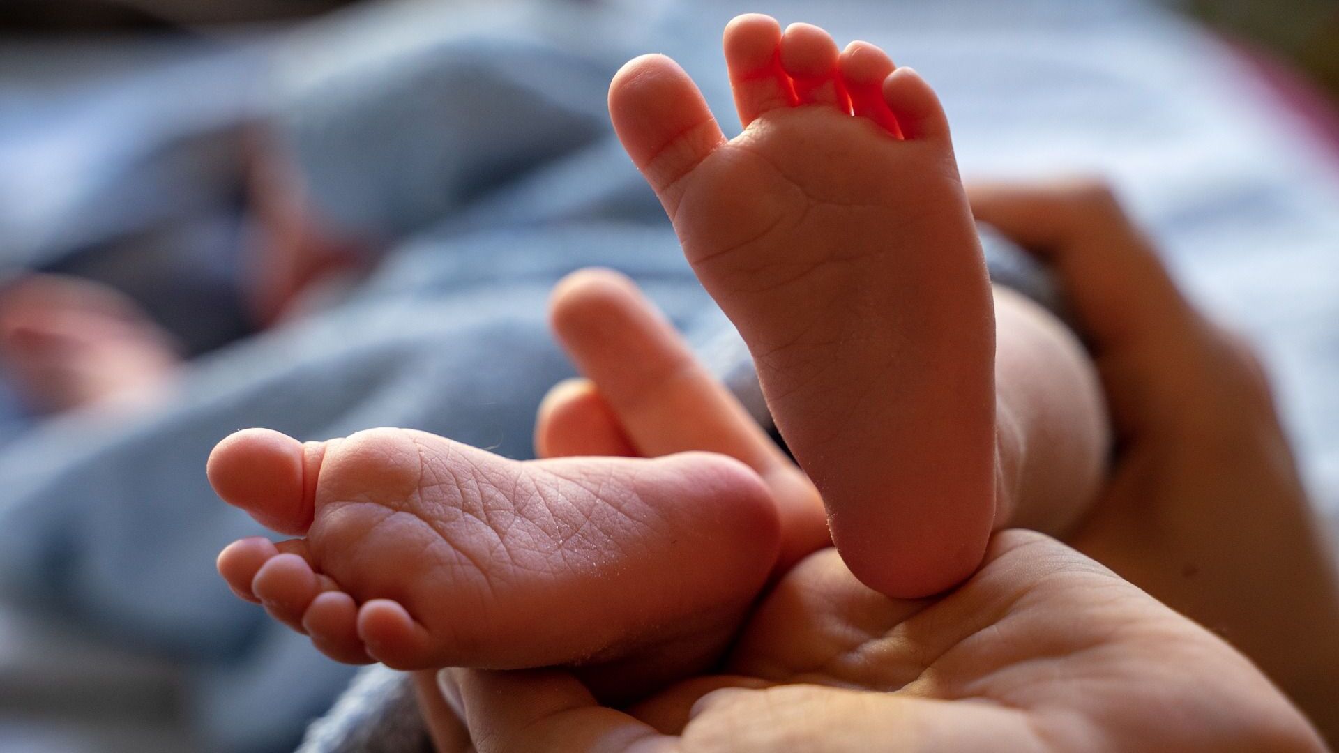 Nahaufnahme von Babyfüßen, die in einer Hand liegen, mit sanften Texturen und weicher Beleuchtung.