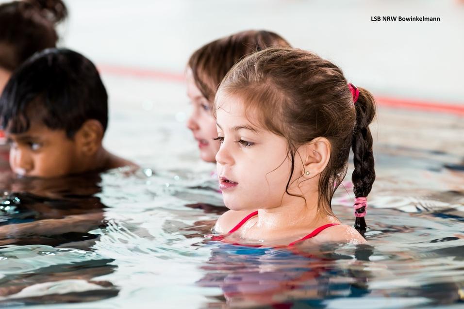 Kinder im Wasser, eine kleine blonde Mädchen mit Zopf in rotem Badeanzug, konzentriert auf das Schwimmen.