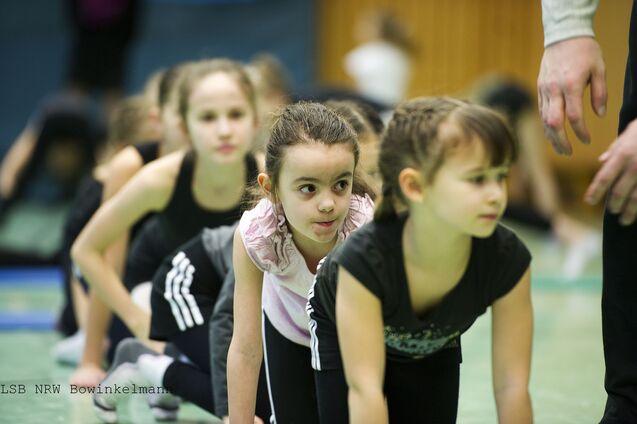 Gruppe von Kindern in Sportkleidung, die sich auf einer Matte in einer Turnstunde konzentrieren.