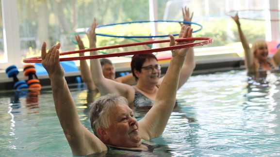 Gruppen von Frauen in einem Schwimmbecken heben Hula-Hoop-Reifen über ihren Köpfen während einer Wasserübungsstunde.