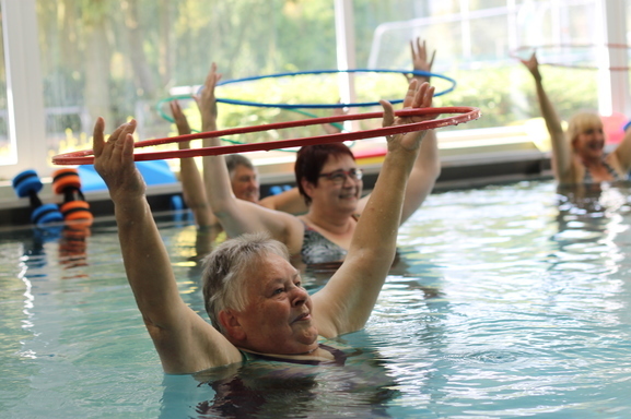 Gruppen von Frauen in einem Schwimmbecken heben Hula-Hoop-Reifen über ihren Köpfen während einer Wasserübungsstunde.