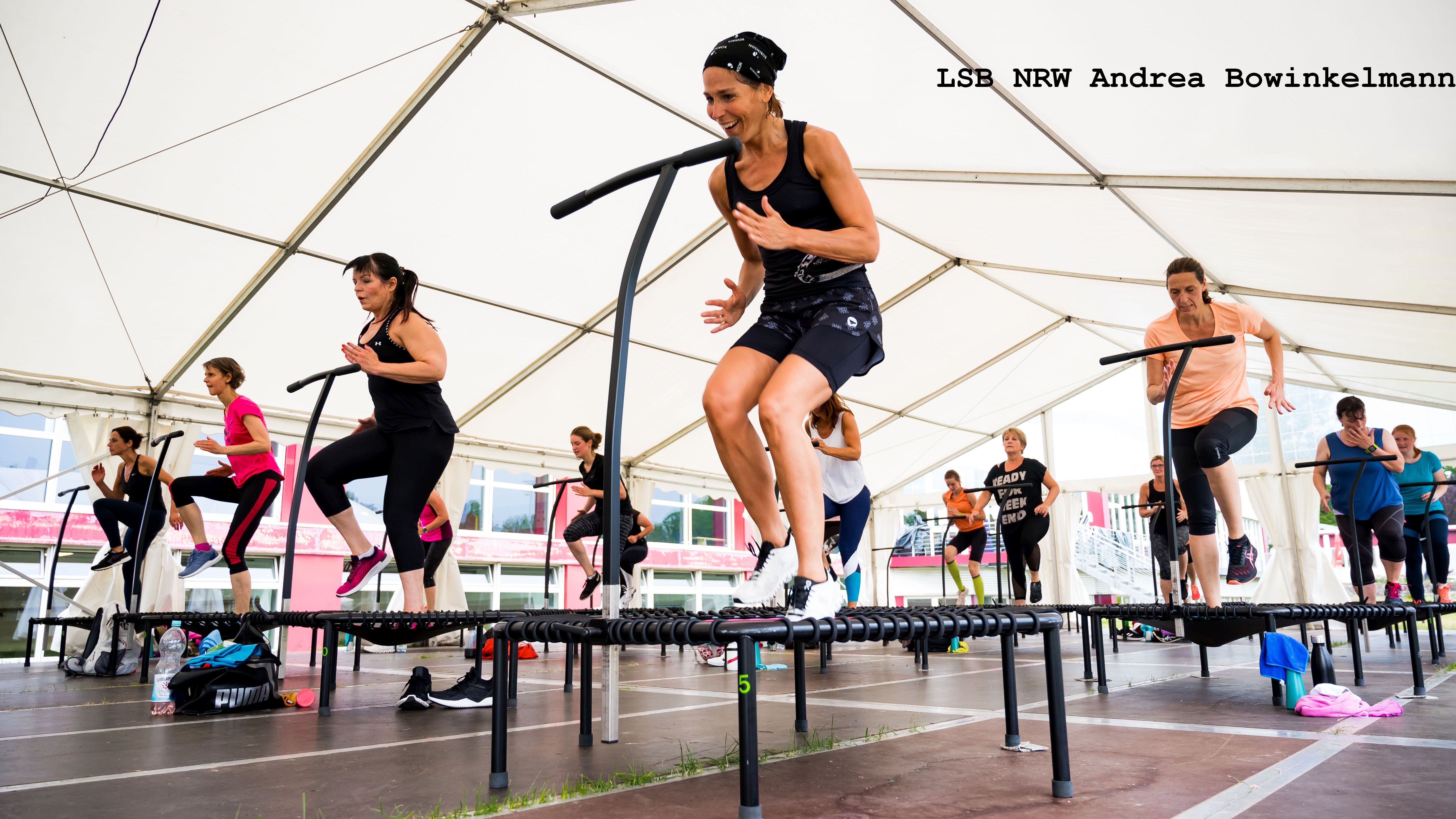 Gruppentraining unter einem Zelt mit mehreren Frauen, die auf Trampolinen springen und sich sportlich betätigen.