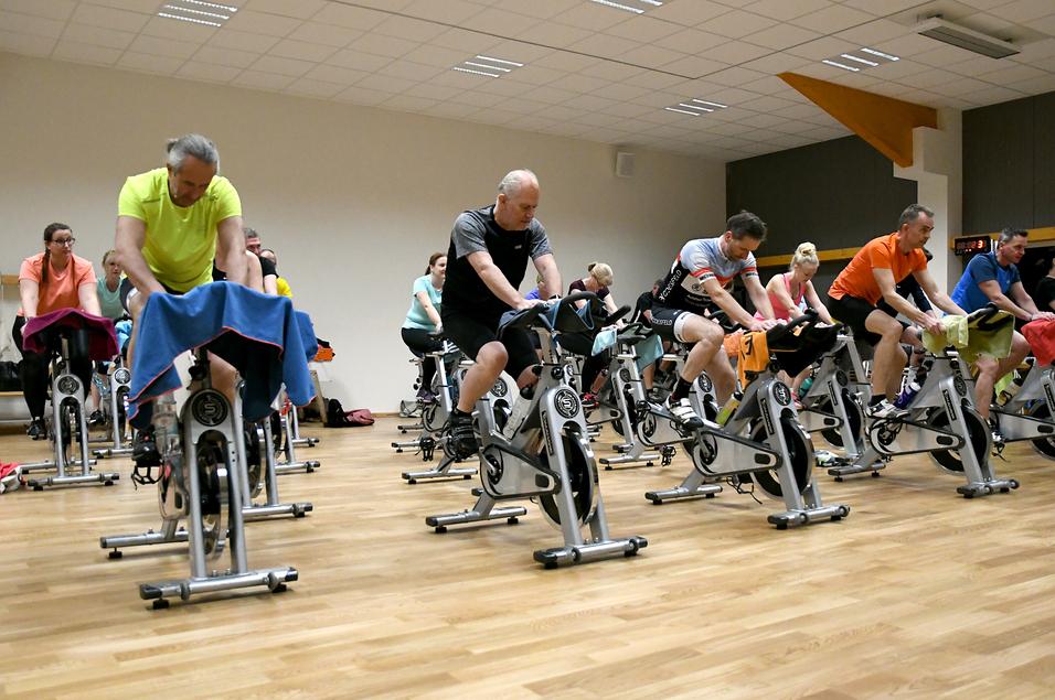 Gruppe von Personen beim Spinning-Kurs, konzentriert auf stationären Fahrrädern in einem modernen Fitnessraum.