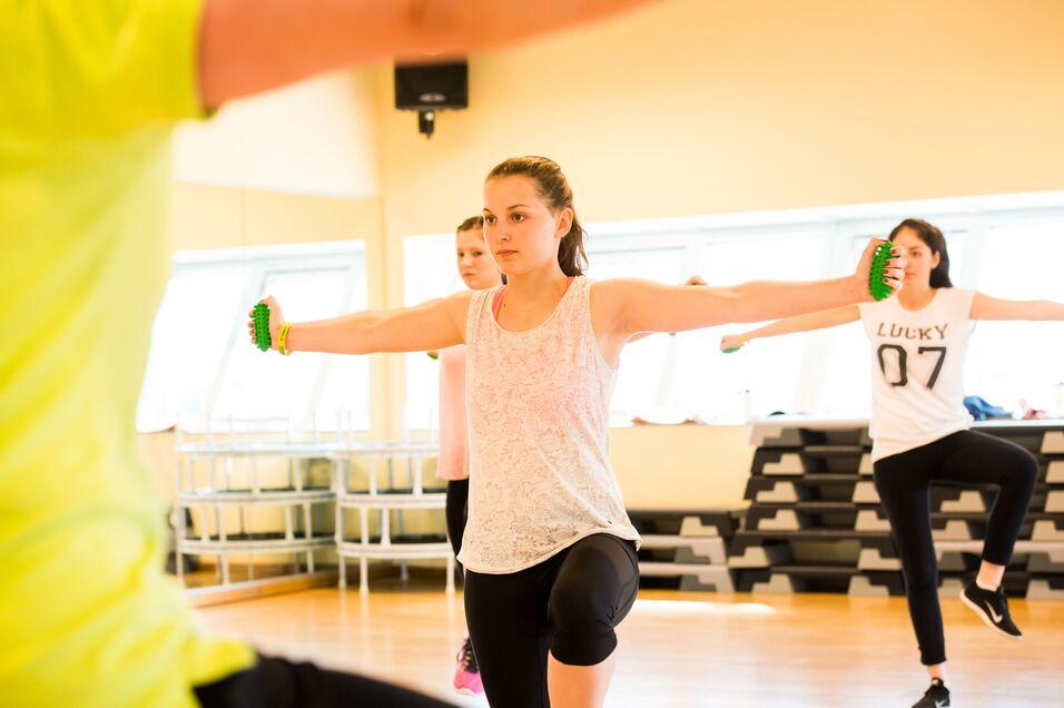 Drei Frauen in Sportkleidung absolvieren ein Workout mit kleinen Gewichten in einem Fitnessraum.