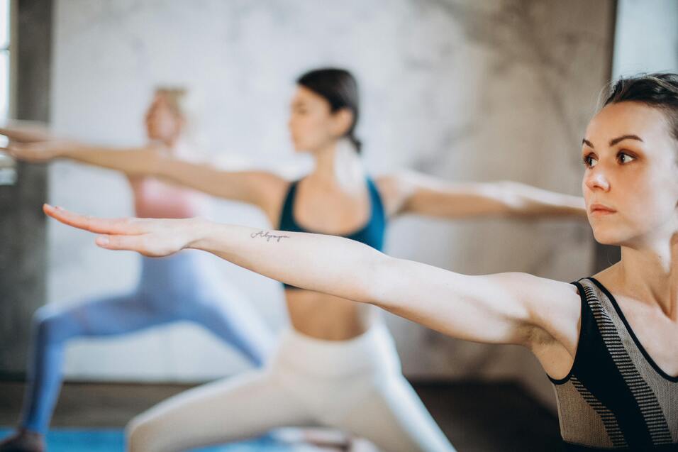 Drei Frauen üben gemeinsam Yoga in einem hellen Raum, während sie in verschiedenen Posen stehen.