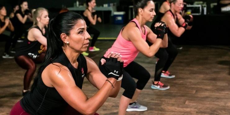 Gruppe von Frauen in Sportkleidung beim Squats-Training in einem Fitnessstudio.