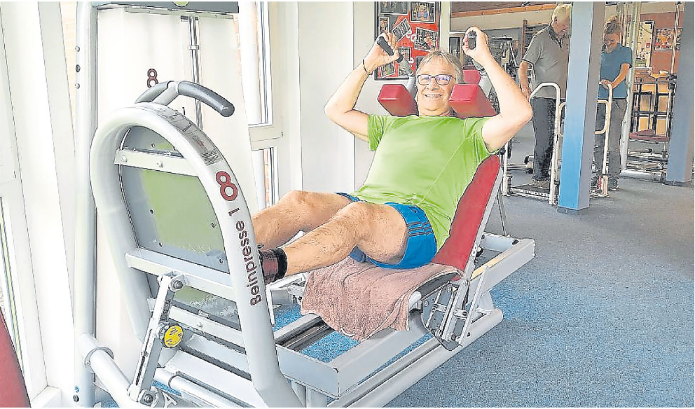 Ein Mann trainiert an einer Beinpresse im Fitnessstudio, lächelt und hält Gewichte mit beiden Händen.