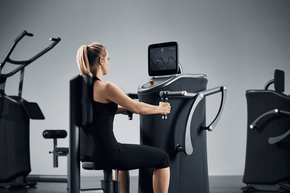 Frau trainiert an einem modernen Fitnessger&auml;t mit Bildschirm in einem modernen Fitnessstudio.