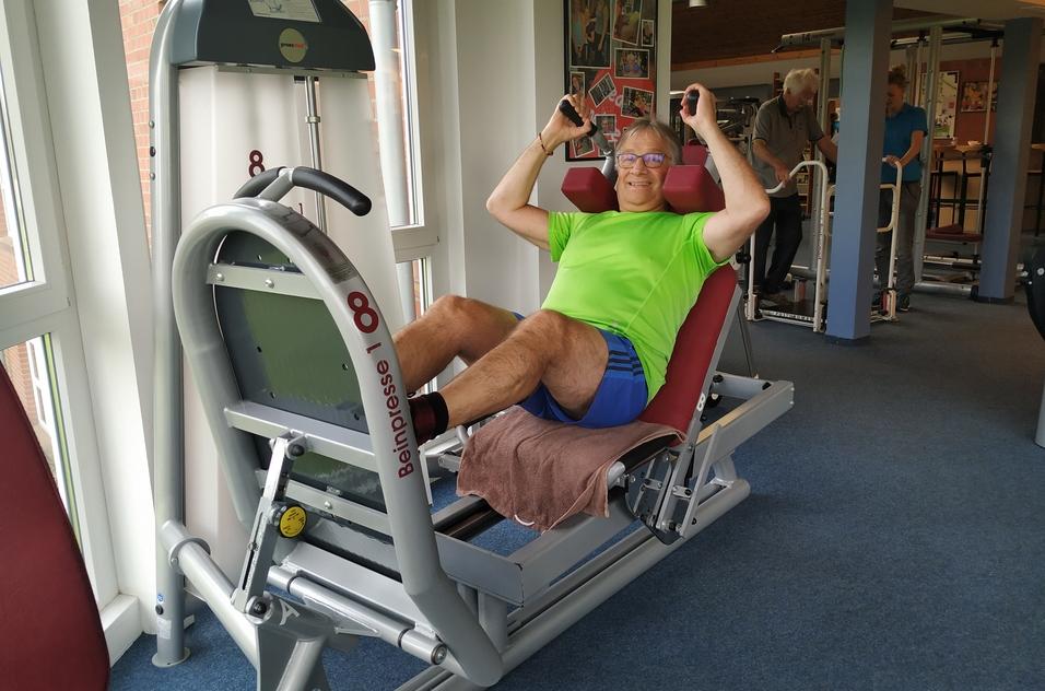 Mann in grünem Shirt trainiert an einer Beinpressmaschine in einem Fitnessstudio.