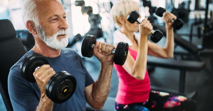 Älteres Paar hebt Gewichte in einem Fitnessstudio, beide konzentriert und aktiv beim Training mit Kurzhanteln.