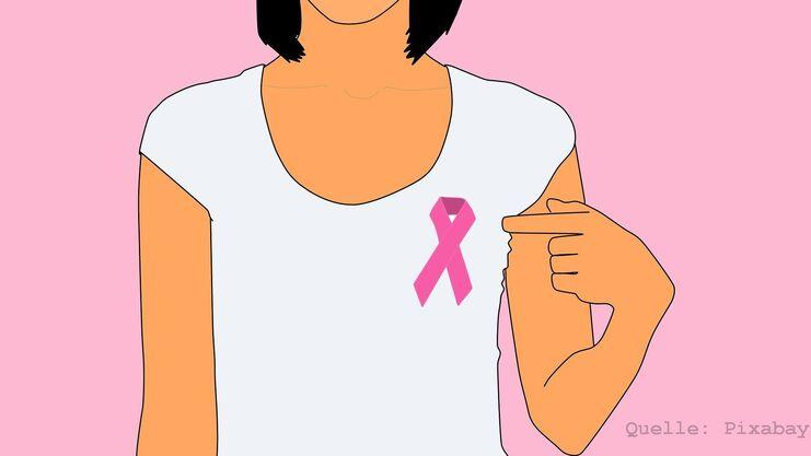 Frau in weißem T-Shirt zeigt auf ein rosa Schleifen-Symbol auf ihrem Oberarm vor pinkem Hintergrund.