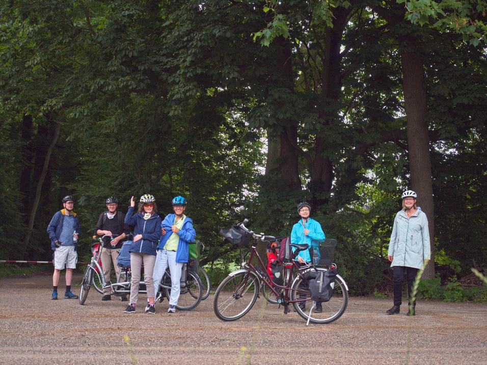 Gruppe von sechs Radfahrern in Fahrrädern, die an einem Waldweg stehen und sich unterhalten.