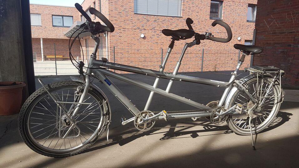 Silbernes Tandemfahrrad mit zwei Sätteln und Lenker, abgestützt in einem schattigen Innenhof.