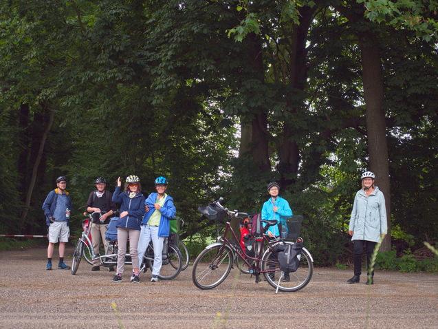 Gruppe von sechs Radfahrern in Fahrrädern, die an einem Waldweg stehen und sich unterhalten.