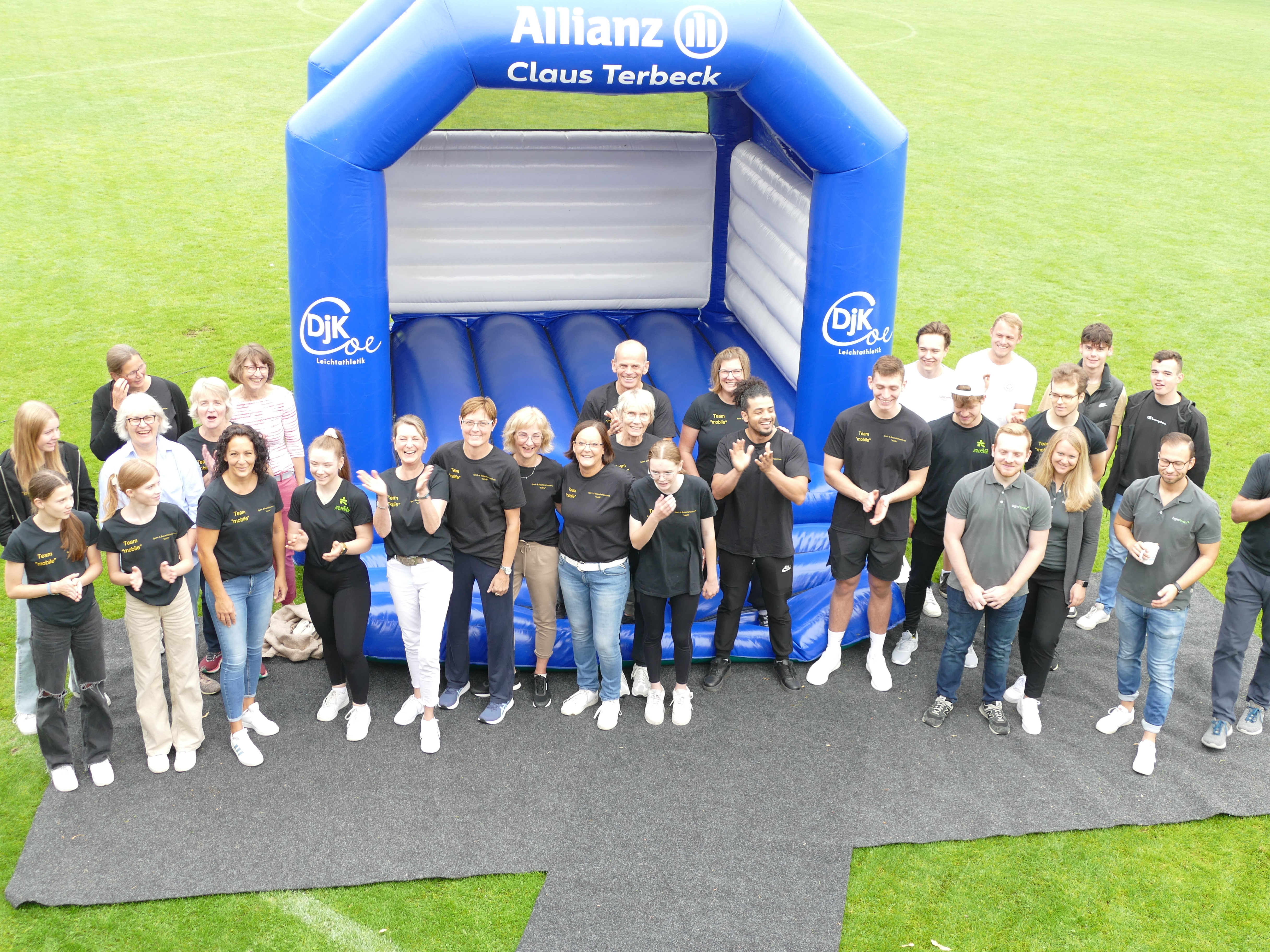 Gruppenfoto von Personen in schwarzen Shirts vor einer Hüpfburg auf einem grünen Rasenplatz.