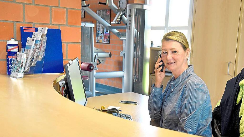 Frau am Empfang telefoniert, umgeben von Informationsmaterialien und Fitnessgeräten in einem modernen Studio.