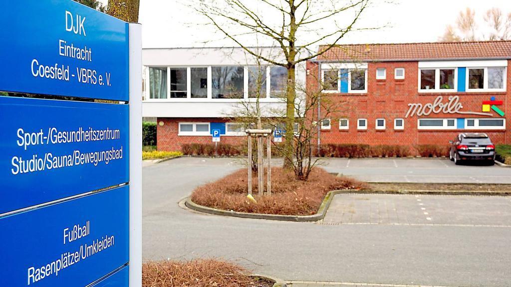 DJK Eintracht Coesfeld: blaues Hinweisschild vor einem Sport- und Gesundheitszentrum mit angrenzendem Parkplatz.