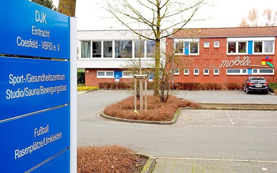 DJK Eintracht Coesfeld: blaues Hinweisschild vor einem Sport- und Gesundheitszentrum mit angrenzendem Parkplatz.