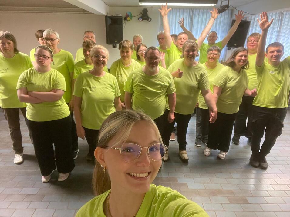 Gruppe von Menschen in leuchtend grünen T-Shirts posiert fröhlich in einem Raum, einige halten die Hände hoch.
