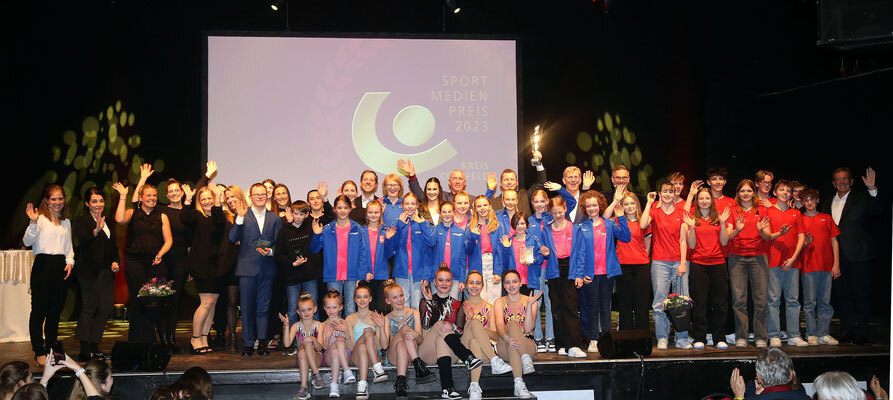 Gruppe von Sportlerinnen und Sportler beim Sport Medien Preis 2023, auf einer Bühne mit Applaus und jubelnden Gesten.