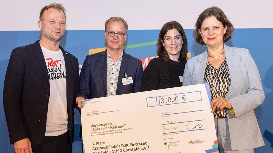 Vier Personen präsentieren einen Scheck über 3.000 Euro für den Vereinspreis „Sport mit Haltung“ in Berlin.