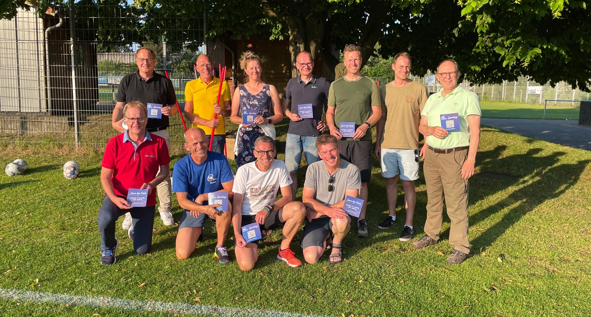 Gruppe von zehn Personen auf einem Sportplatz, alle halten Zertifikate in den Händen. Im Hintergrund Fußball und Bäume.