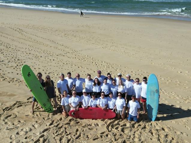 Gruppe von Surfern in weißen T-Shirts auf dem Sandstrand, umgeben von Surfboards in grün, rot und blau.