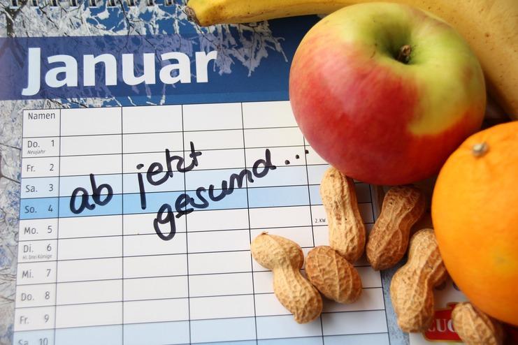 Kalenderblatt für Januar mit der handschriftlichen Notiz „ab jetzt gesund“ und frischem Obst: Apfel, Banane, Orange, Erdnüsse.