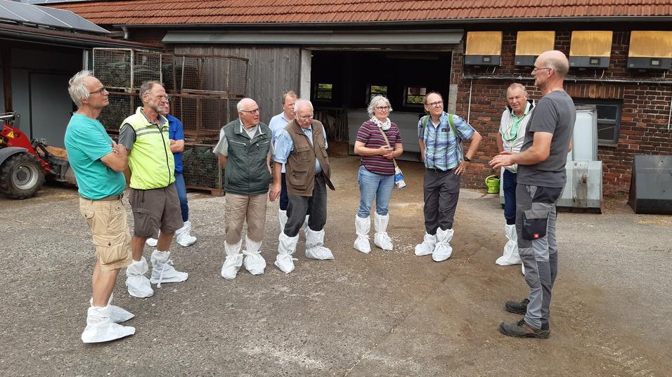 Gruppe von sechs Personen in Schuhe gehüllt, lauscht einem Mann vor einem Weidezelt mit Photovoltaikanlage.