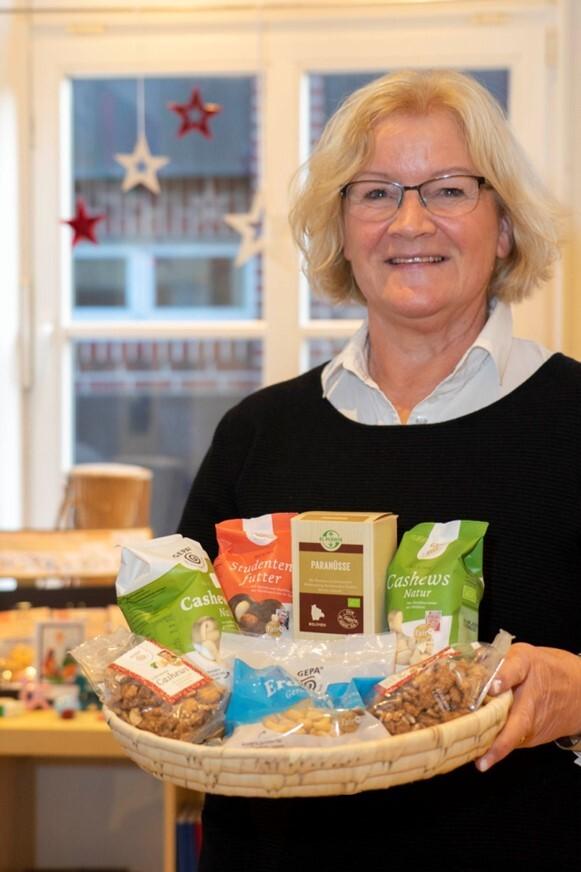 Frau mit Brille hält einen Korb voller Nussprodukte und Snacks vor einem hellen Hintergrund mit Weihnachtsdekoration.