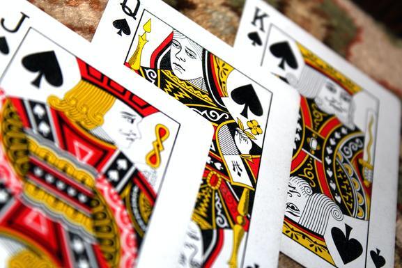 Nahaufnahme von drei Spielkarten: König, Dame und Bube der Pik-Farbe, mit detaillierten Illustrationen.