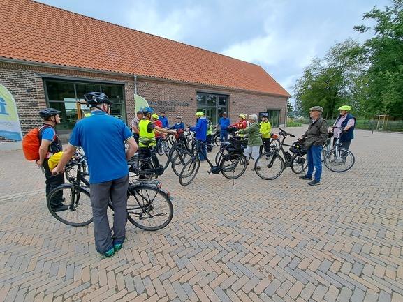 Gruppe von Radfahrern in Helmen, die sich mit Fahrrädern auf einem Platz vor einem Gebäude versammelt haben.