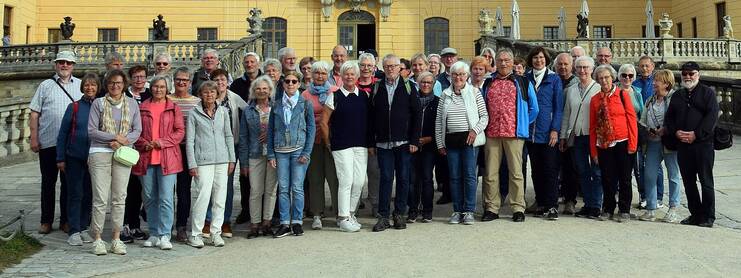 Gruppe von 49 Menschen posiert vor einem historischen Gebäude mit Geländer auf einem Platz im Freien.